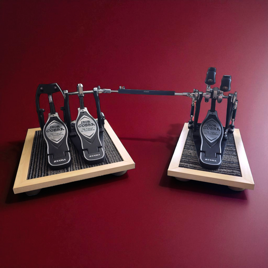 Maple silent stomper isolation platforms (single drum pedal and double drum pedal pack) installed on a drum set. It is designed for drummers, enabling quiet practice in enclosed spaces like apartment buildings by reducing vibrations and preventing noise disturbances and complaints from neighbors.