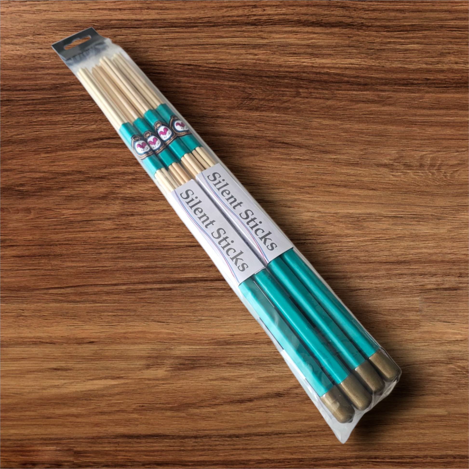 A package containing two pairs of custom Silent Sticks 7-dowel hot rod drumsticks with green grip and gold end caps. Low volume practice drum rods for apartments and low-volume acoustic gigs.