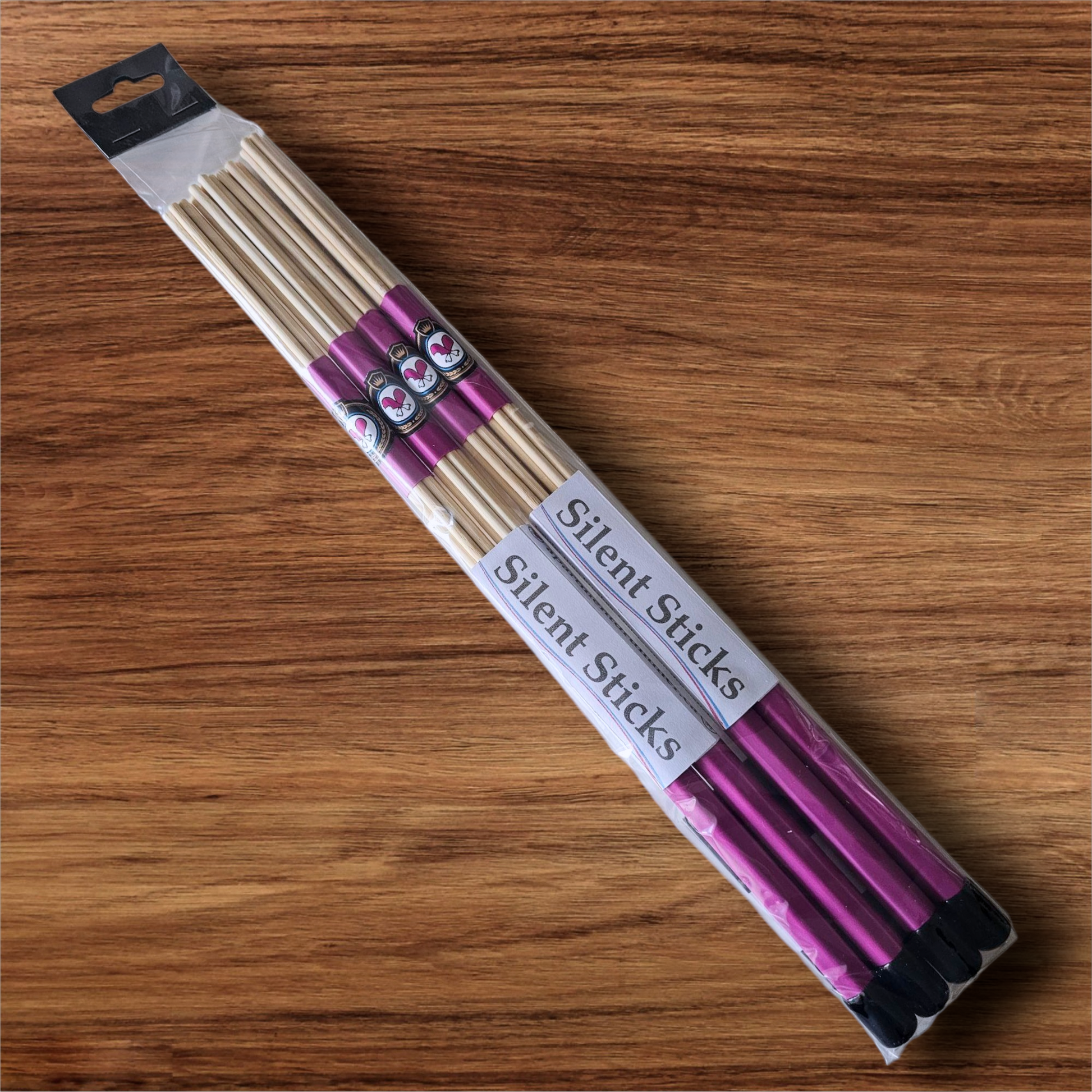 A package containing two pairs of custom Silent Sticks 7-dowel hot rod drumsticks with pink grip and black end caps. Low volume practice drum rods for apartments and low-volume acoustic gigs.