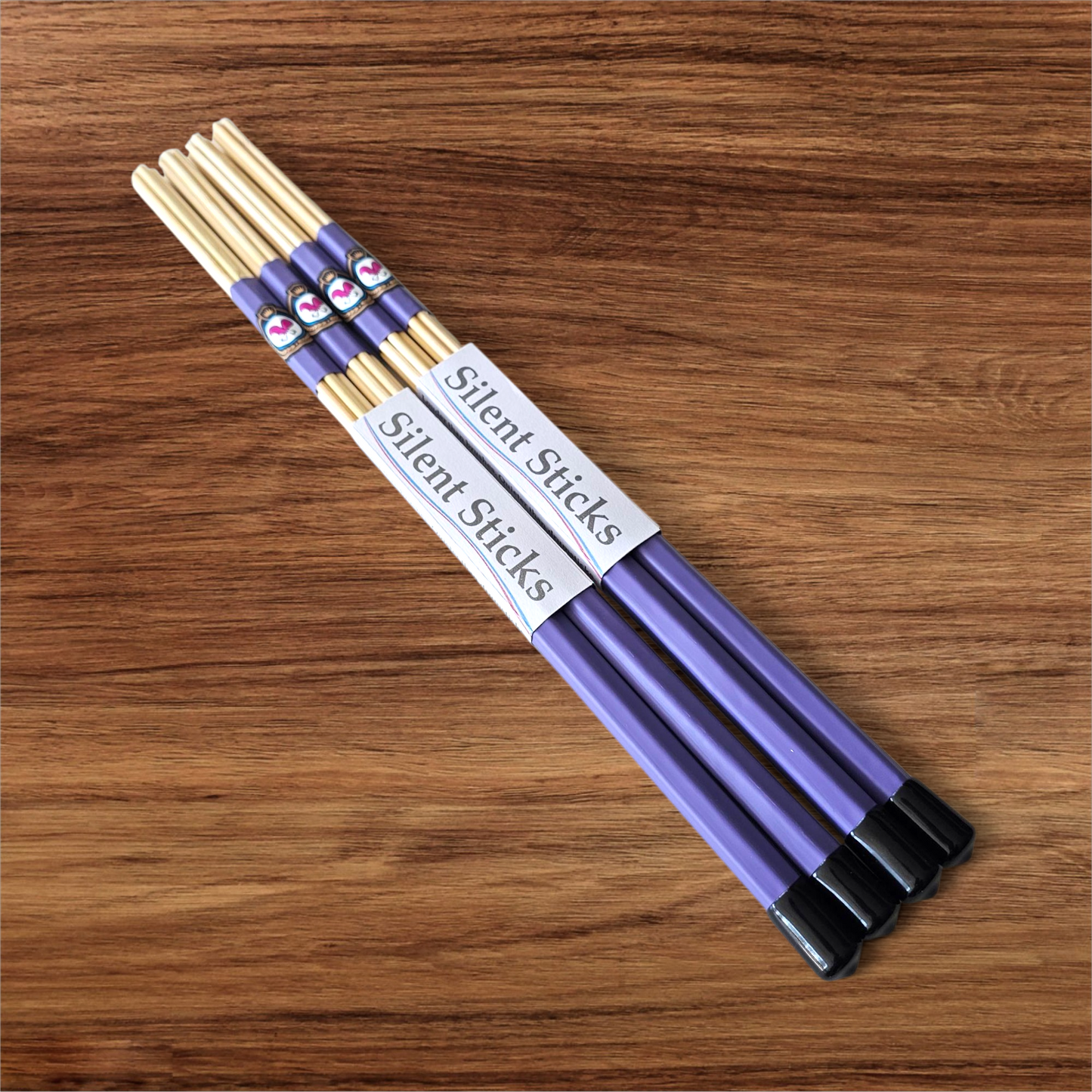 A package containing two pairs of custom Silent Sticks 7-dowel hot rod drumsticks with purple grip and black end caps. Low volume practice drum rods for apartments and low-volume acoustic gigs.