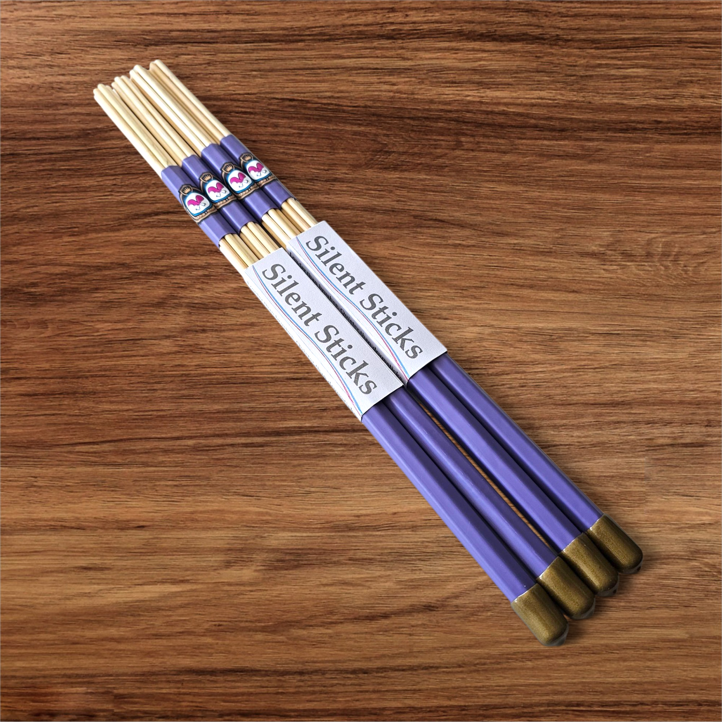 A package containing two pairs of custom Silent Sticks 7-dowel hot rod drumsticks with purple grip and gold end caps. Low volume practice drum rods for apartments and low-volume acoustic gigs.