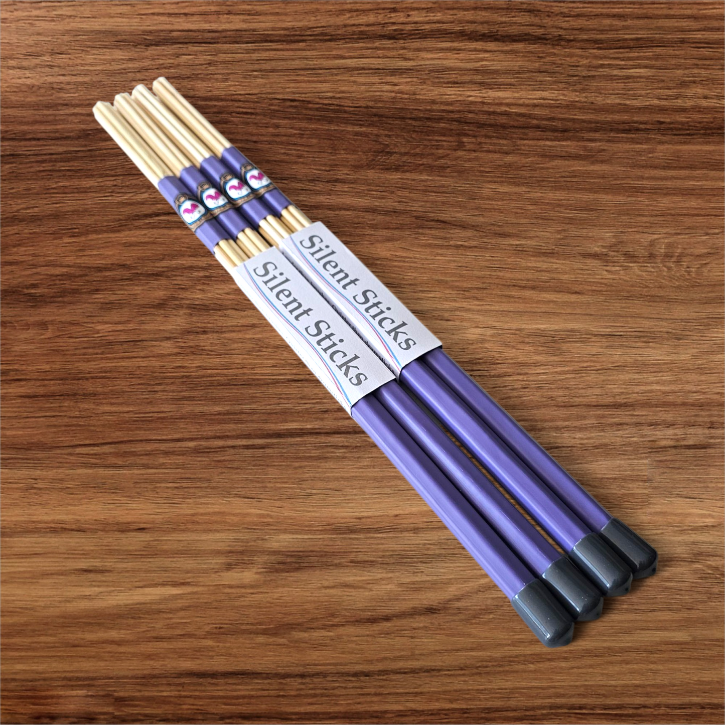 A package containing two pairs of custom Silent Sticks 7-dowel hot rod drumsticks with purple grip and grey end caps. Low volume practice drum rods for apartments and low-volume acoustic gigs.