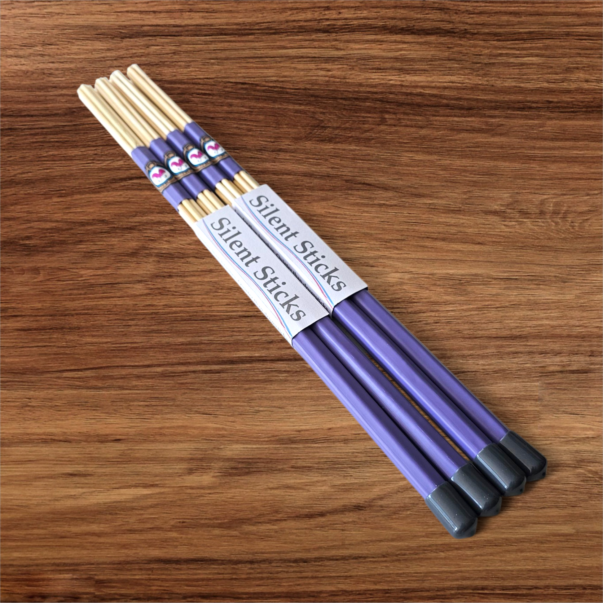 A package containing two pairs of custom Silent Sticks 7-dowel hot rod drumsticks with purple grip and grey end caps. Low volume practice drum rods for apartments and low-volume acoustic gigs.