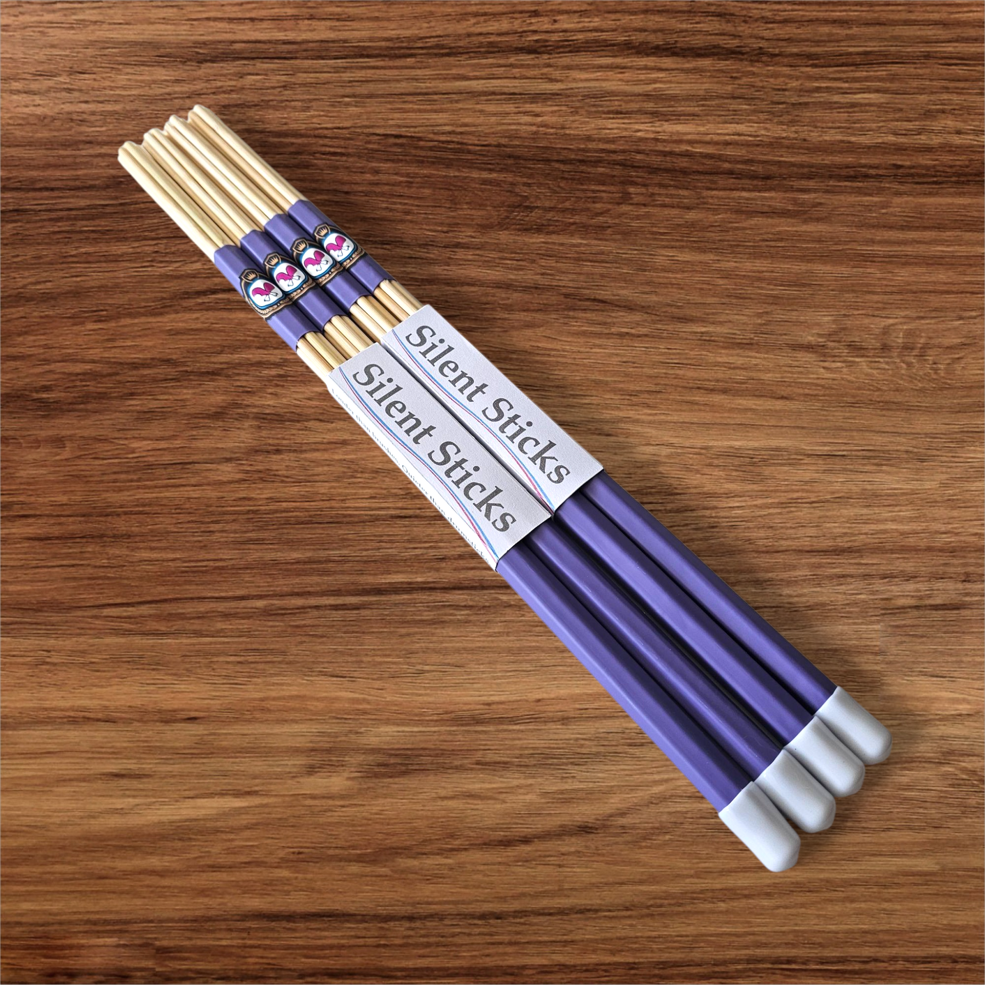 A package containing two pairs of custom Silent Sticks 7-dowel hot rod drumsticks with purple grip and white end caps. Low volume practice drum rods for apartments and low-volume acoustic gigs.