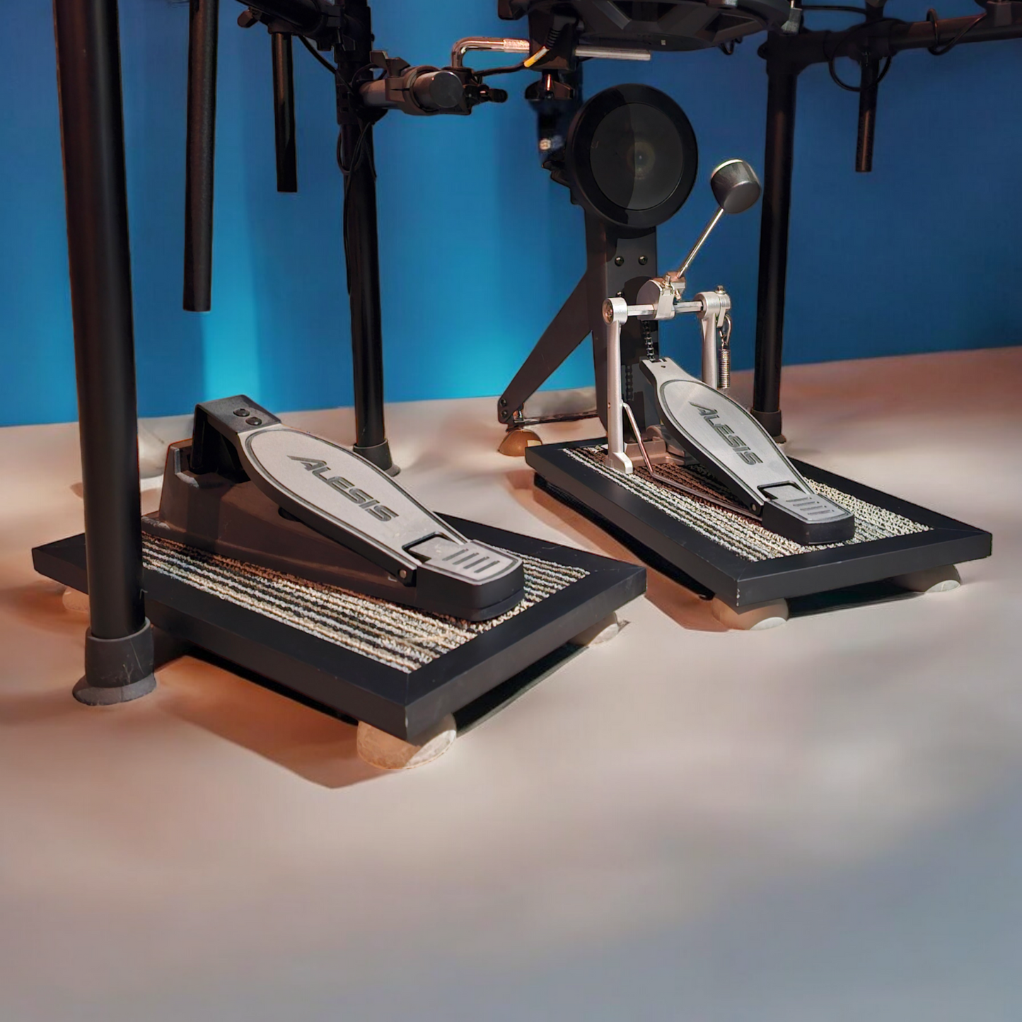 A pair of black Silent Stomper impact noise isolation platforms mounted onto an electric drumset (single pedal pack of two - for hi-hat pedals and bass drum pedals) designed for drummers, enabling quiet practice in enclosed spaces like apartment buildings by reducing vibrations and preventing noise disturbances/complaints for neighbors.