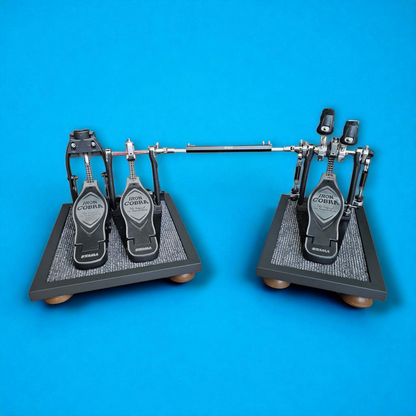 A pair of grey Silent Stomper impact noise isolation platforms (single pedal and double pedal pack - for hi-hat pedals and double bass drum pedals) designed for drummers, enabling quiet practice in enclosed spaces like apartment buildings by reducing vibrations and preventing noise disturbances/complaints for neighbors.